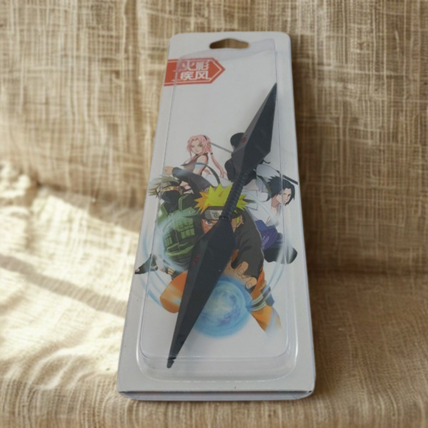 Naruto-inspired Kusuna Kunai Knife with dual black blades and red Leaf Village symbol, placed on a Naruto-themed background