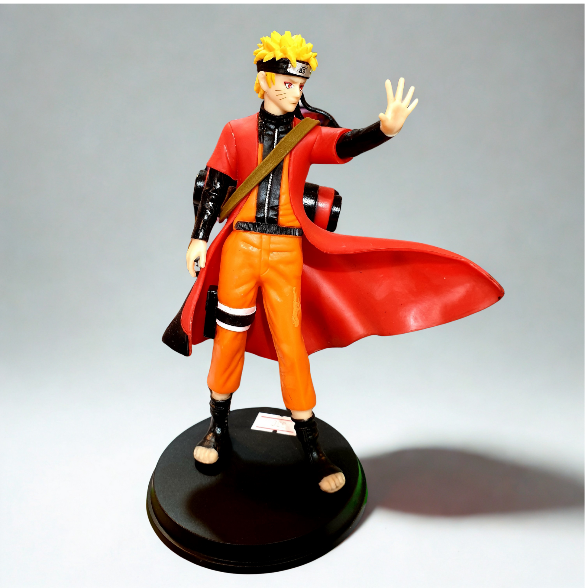 Naruto Uzumaki standing figure with red cloak, orange jumpsuit, and black ninja sandals on a round base.