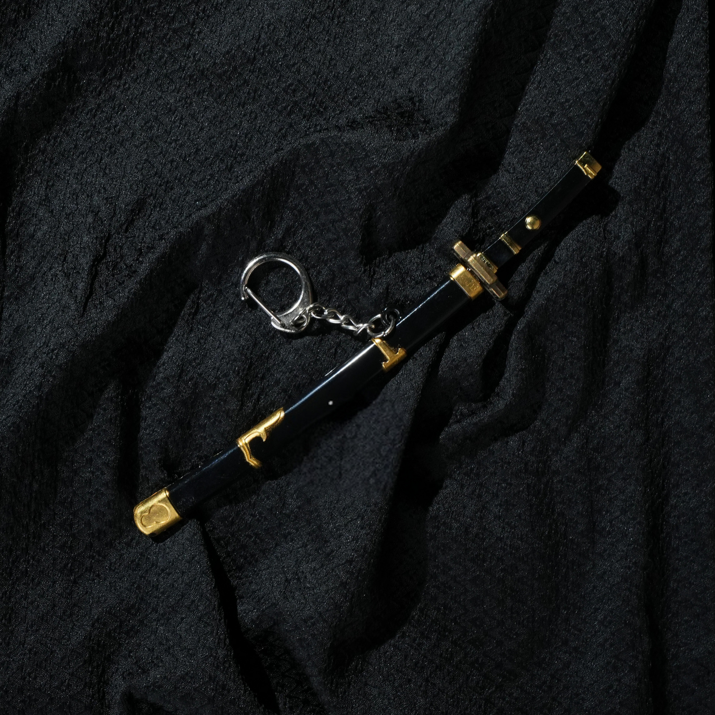 Black and gold Yubashiri katana keychain inspired by One Piece's Roronoa Zoro, placed on a dark fabric background