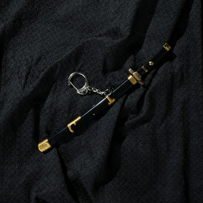 Black and gold Yubashiri katana keychain inspired by One Piece's Roronoa Zoro, placed on a dark fabric background