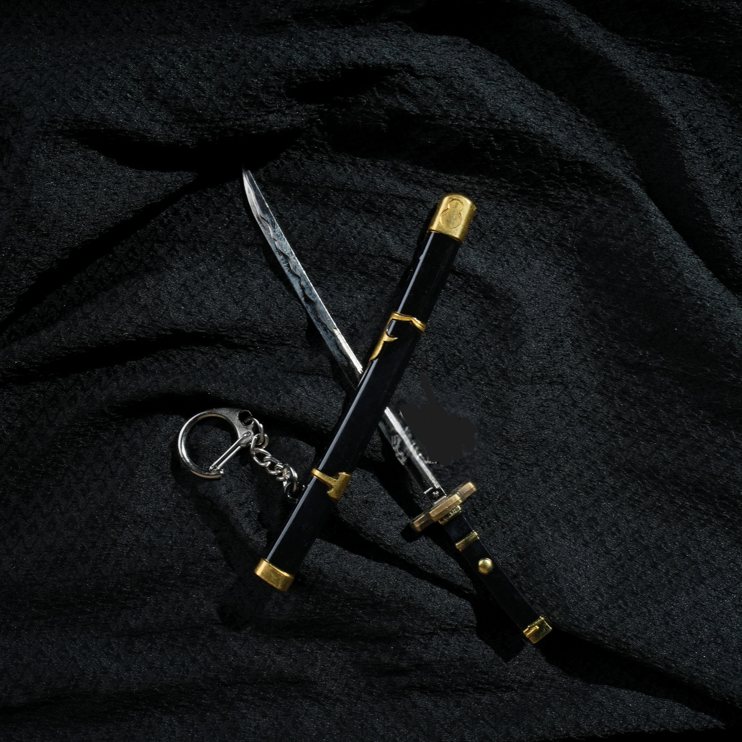 Black and gold Yubashiri katana keychain inspired by One Piece's Roronoa Zoro, placed on a dark fabric background