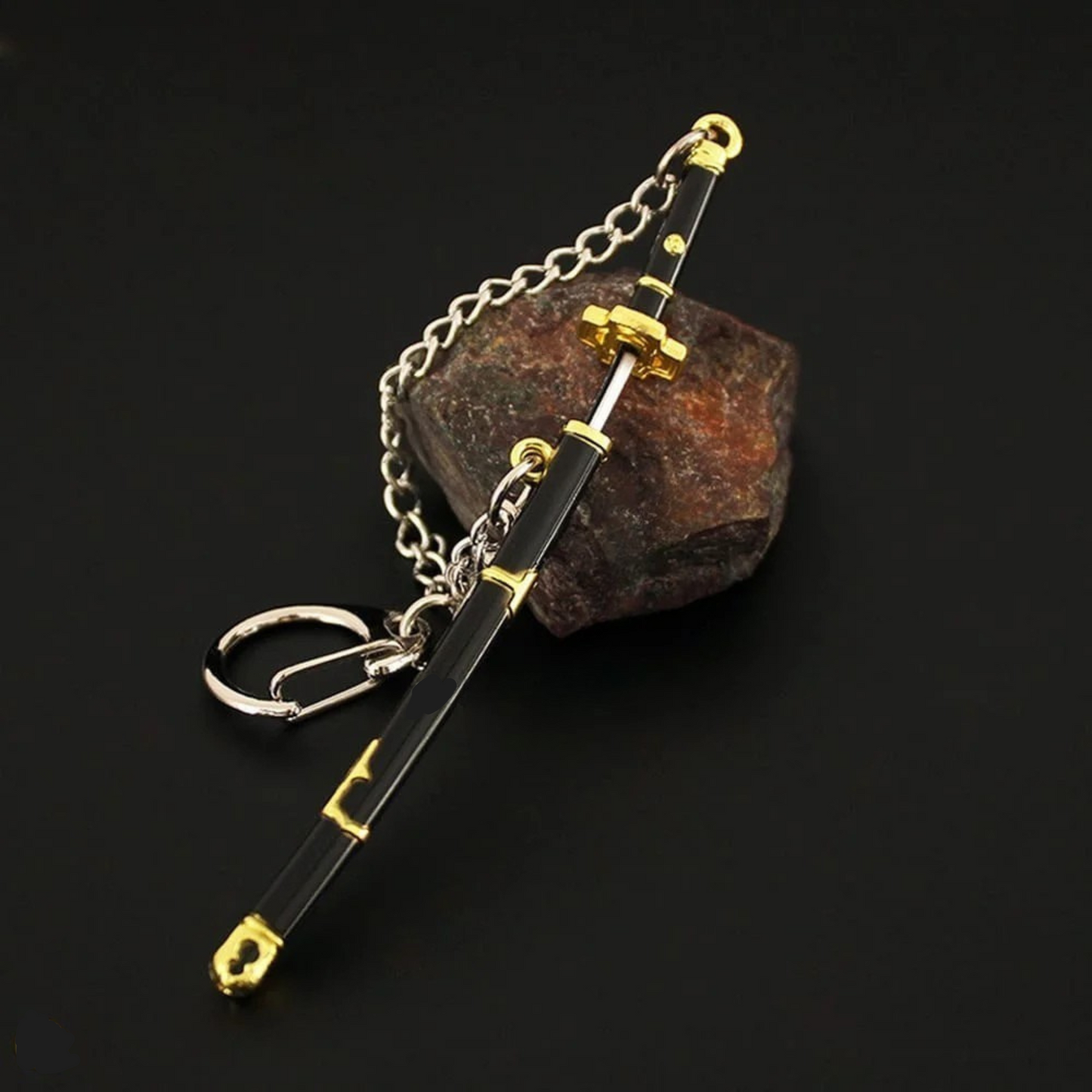 Black and gold Yubashiri katana keychain inspired by One Piece's Roronoa Zoro, placed on a dark fabric background